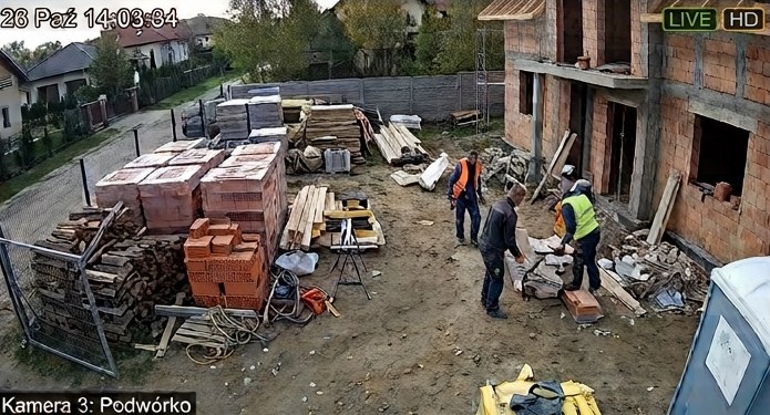 Podgląd kamery: podwórko z materiałami budowlanymi i ekipą